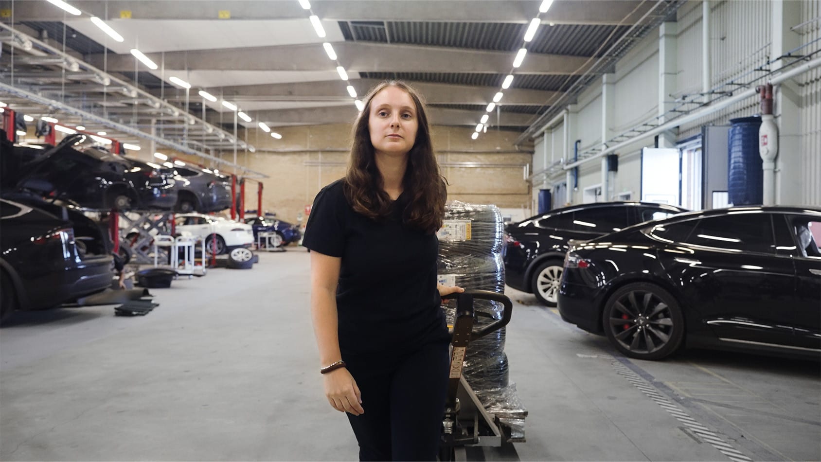 Female Tesla employee pulling a pallet truck in a Tesla warehouse