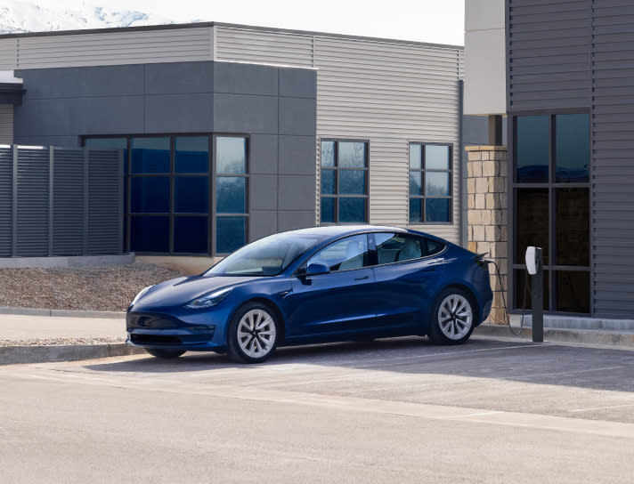 Blue Model 3 charging in a parking lot with a Wall Connector