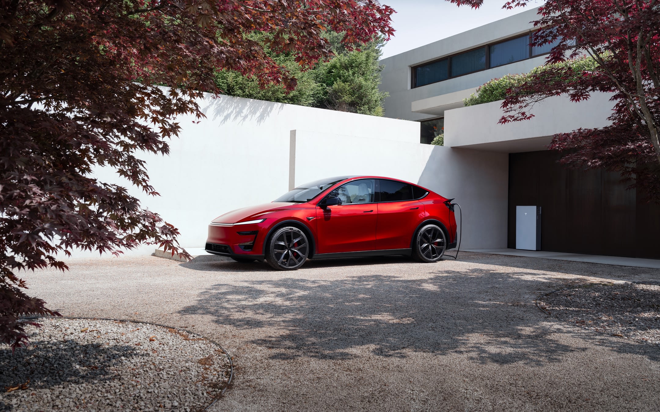 Ultra Red Model Y charging with a Wall Connector in front of a residential garage