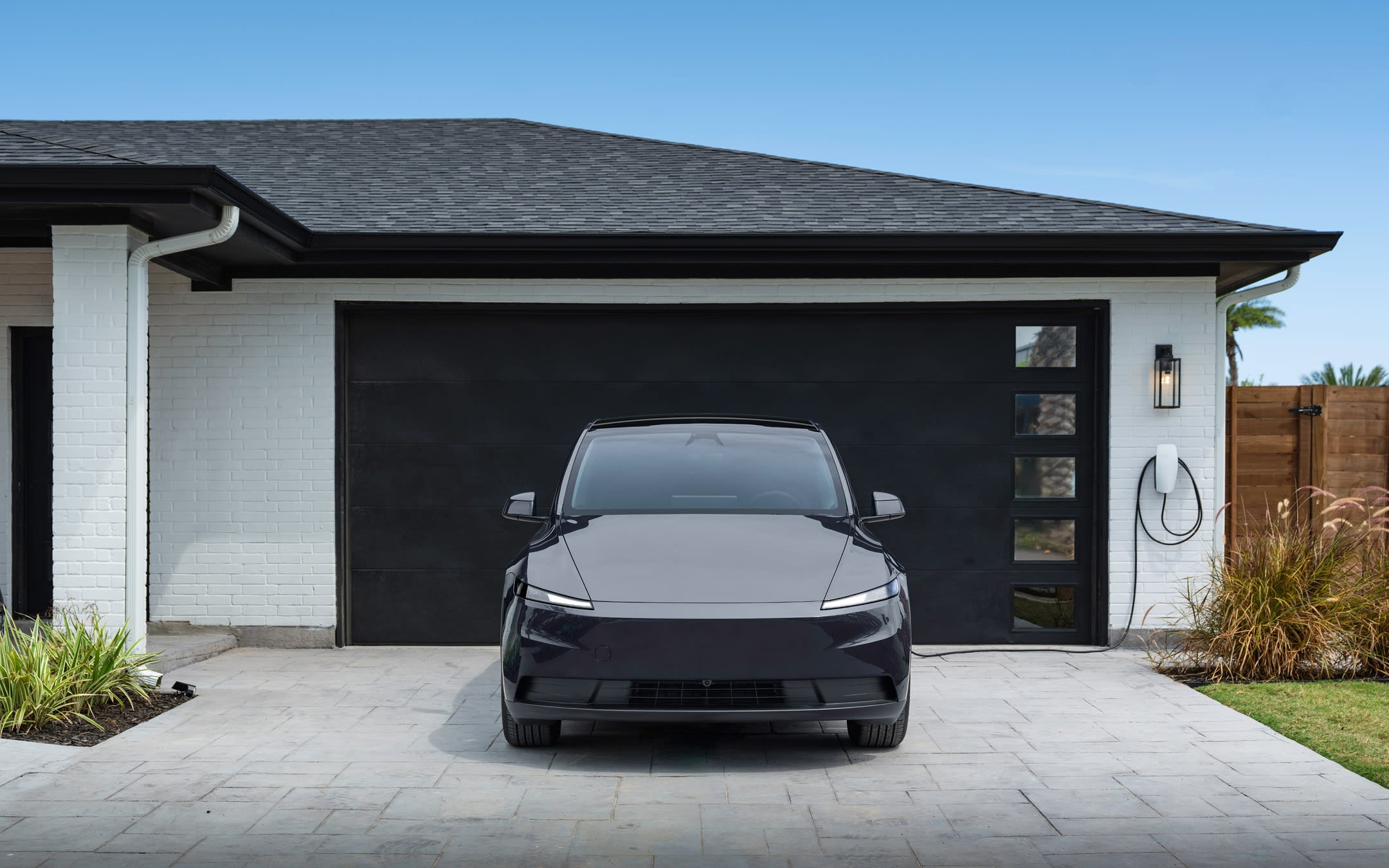 Black Model Y charging at a Wall Connector in front of a residential garage