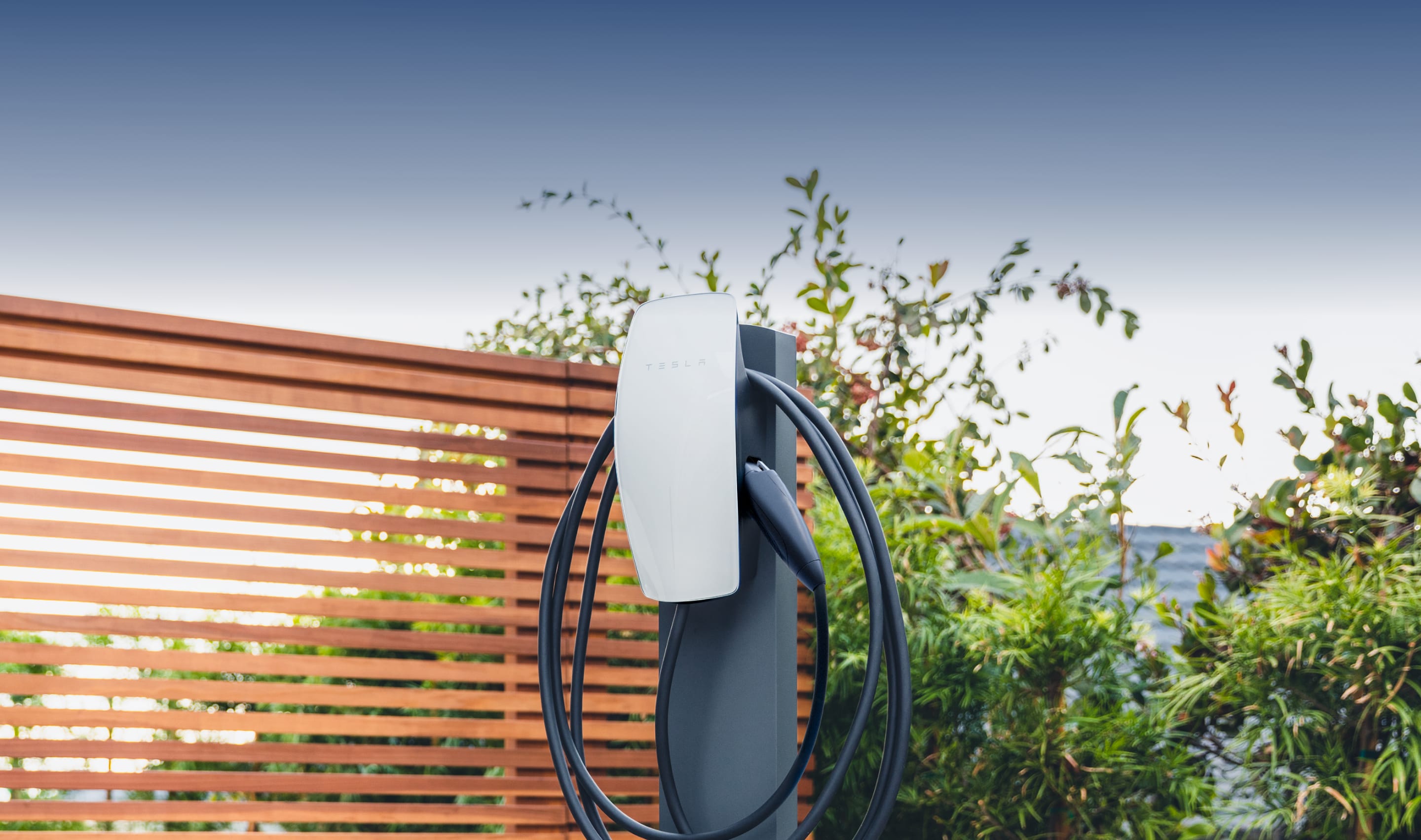 Gen 3 Wall Connector with tempered white glass faceplate mounted on a pedestal in front of a fence