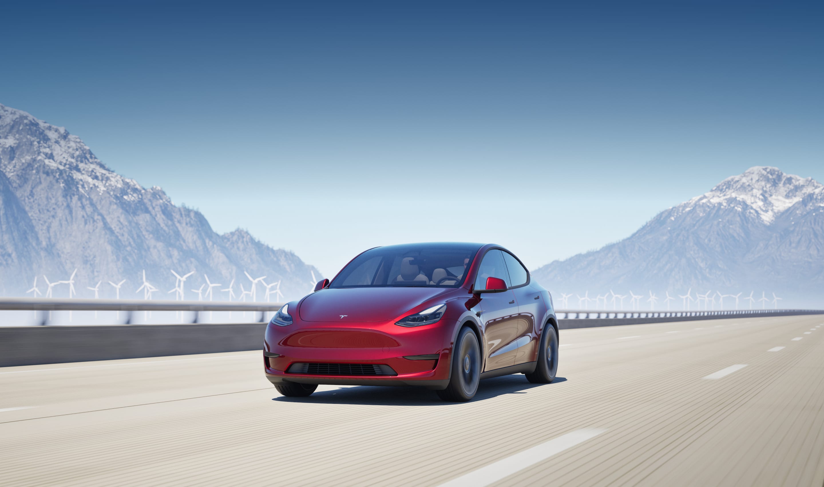 Ultra Red New Model Y driving next to a Quicksilver Model Y on a highway surrounded by windmills and mountains