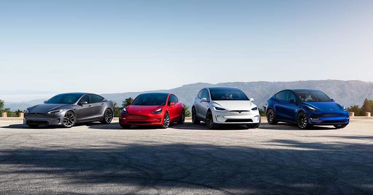 A grey Model S, a red Model 3, a white Model X and a blue Model Y parked on the road in a mountain landscape