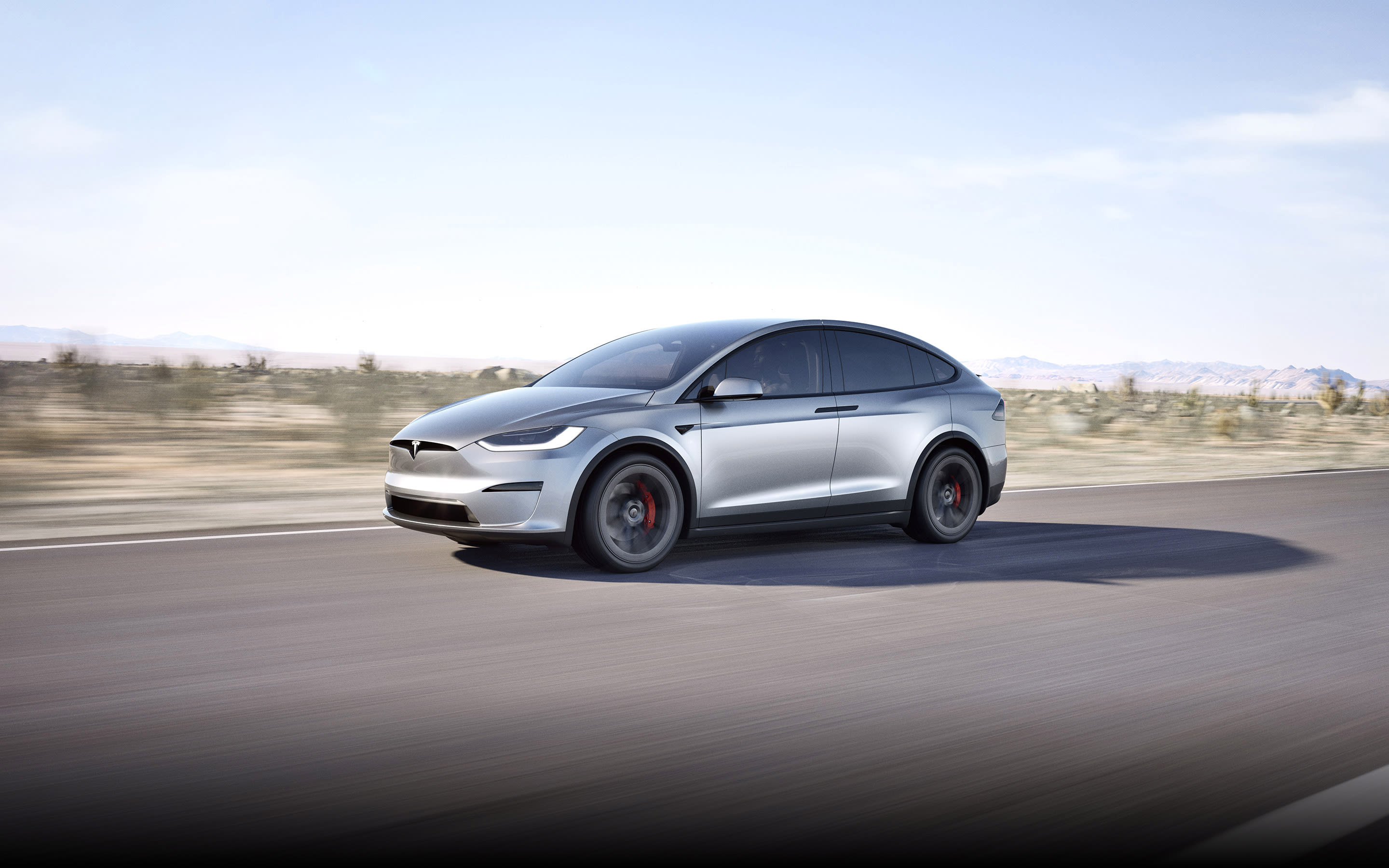 Model X Plaid Blanco Perla conduciendo por una carretera con montañas al fondo