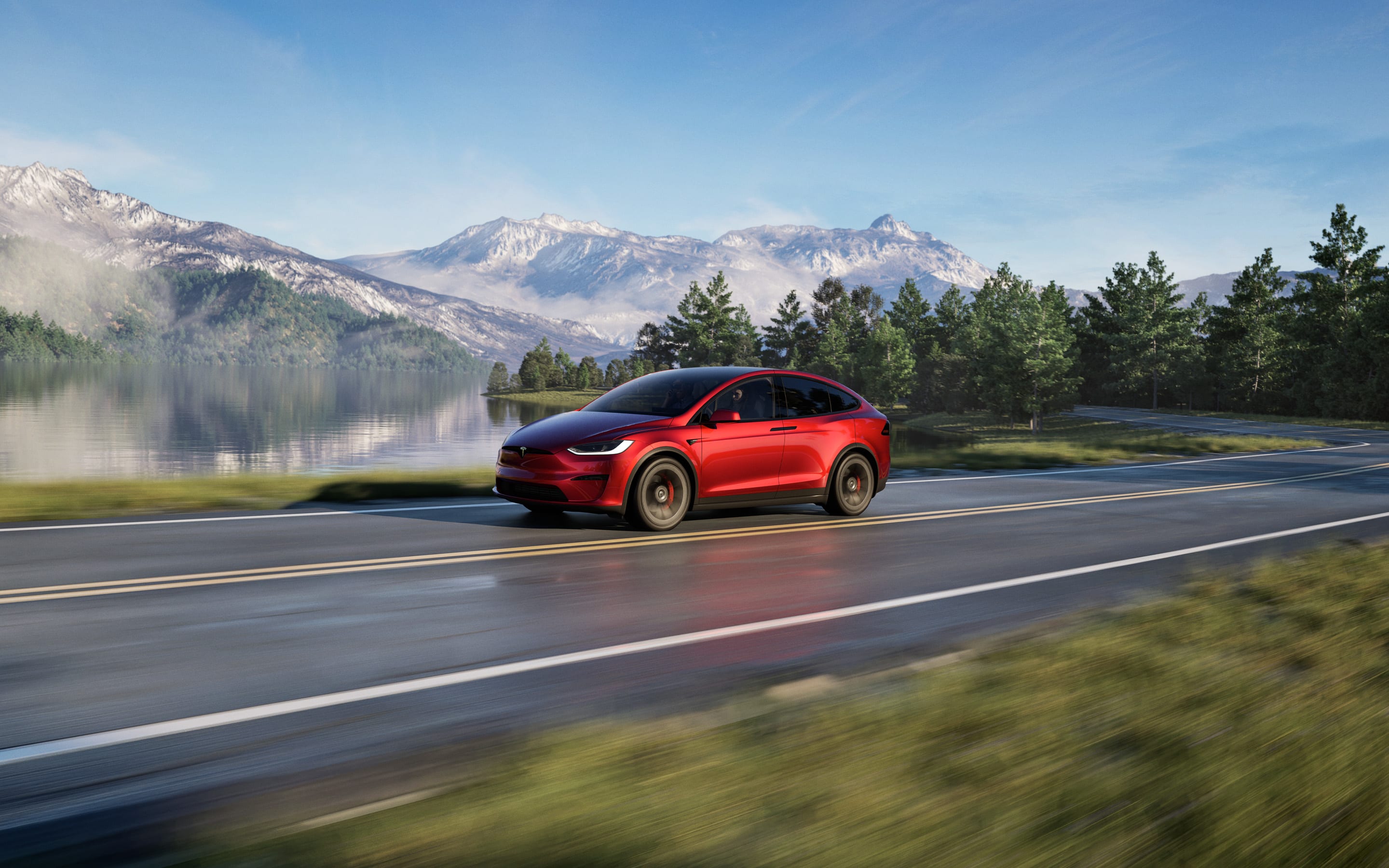 A red Model X Plaid accelerating down a highway with a lake and snow-covered mountains in the background