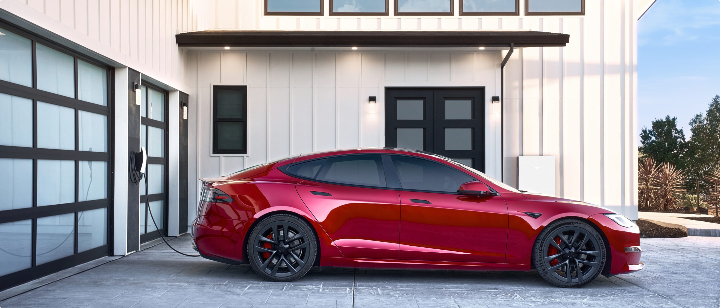 Red Model S being charged with a Wall Connector outside of a garage