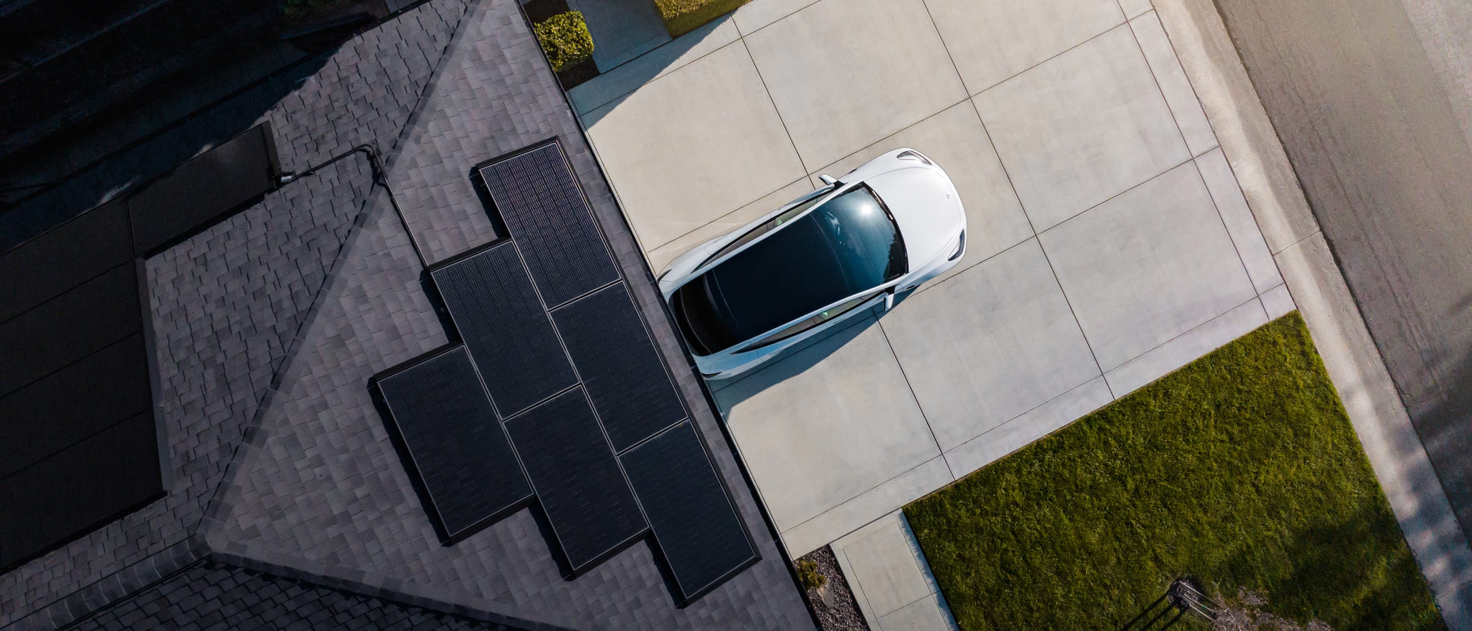 An aerial of a home with solar panels and a parked white Tesla vehicle