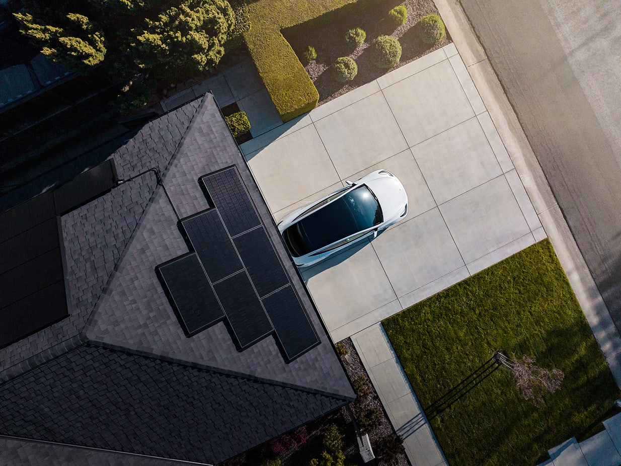 Aerial view of a home with solar panels and white Model Y parked outside a home