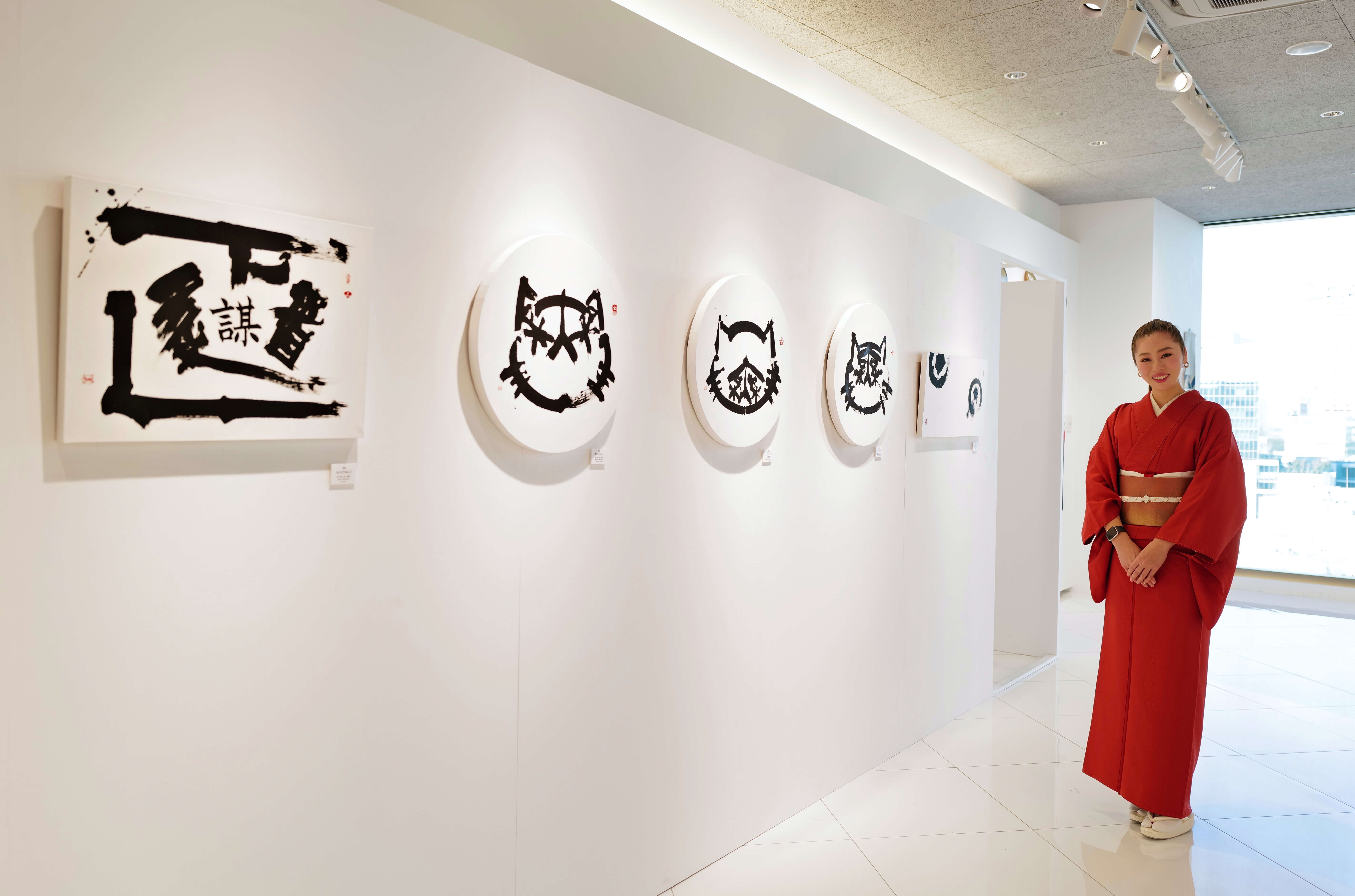 Tesla owner in red kimono standing next to her Japanese calligraphy artwork in a white room