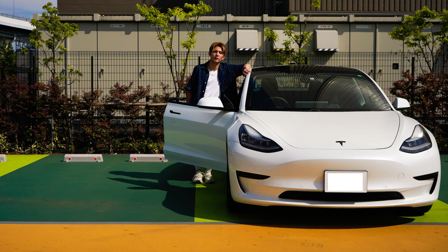 A Tesla owner standing next to a white Model 3 with the driver's door open in a parking lot