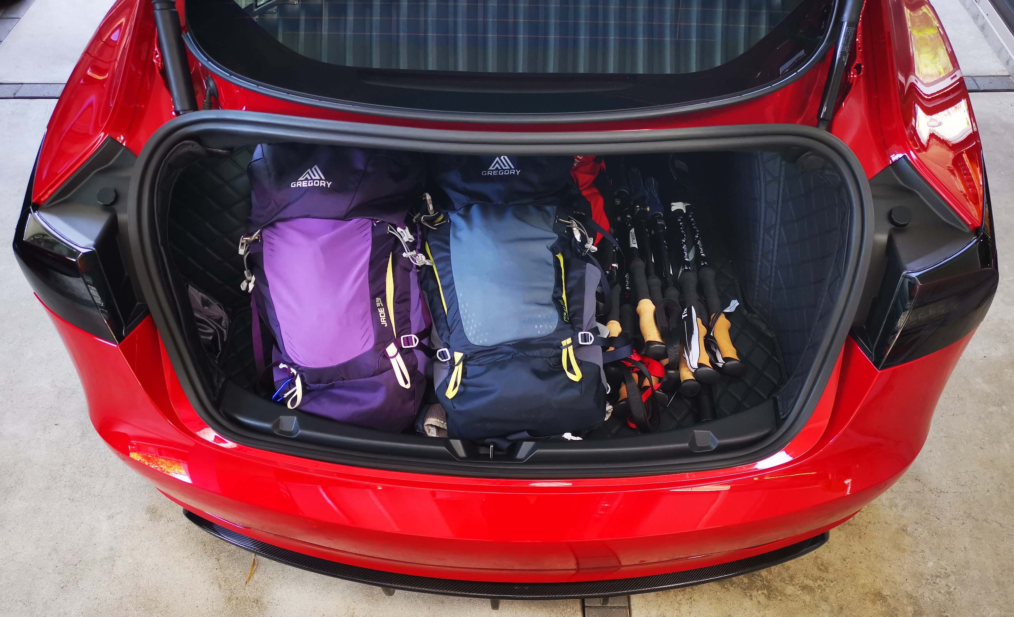 Hiking bags and poles in the rear trunk of red Model 3