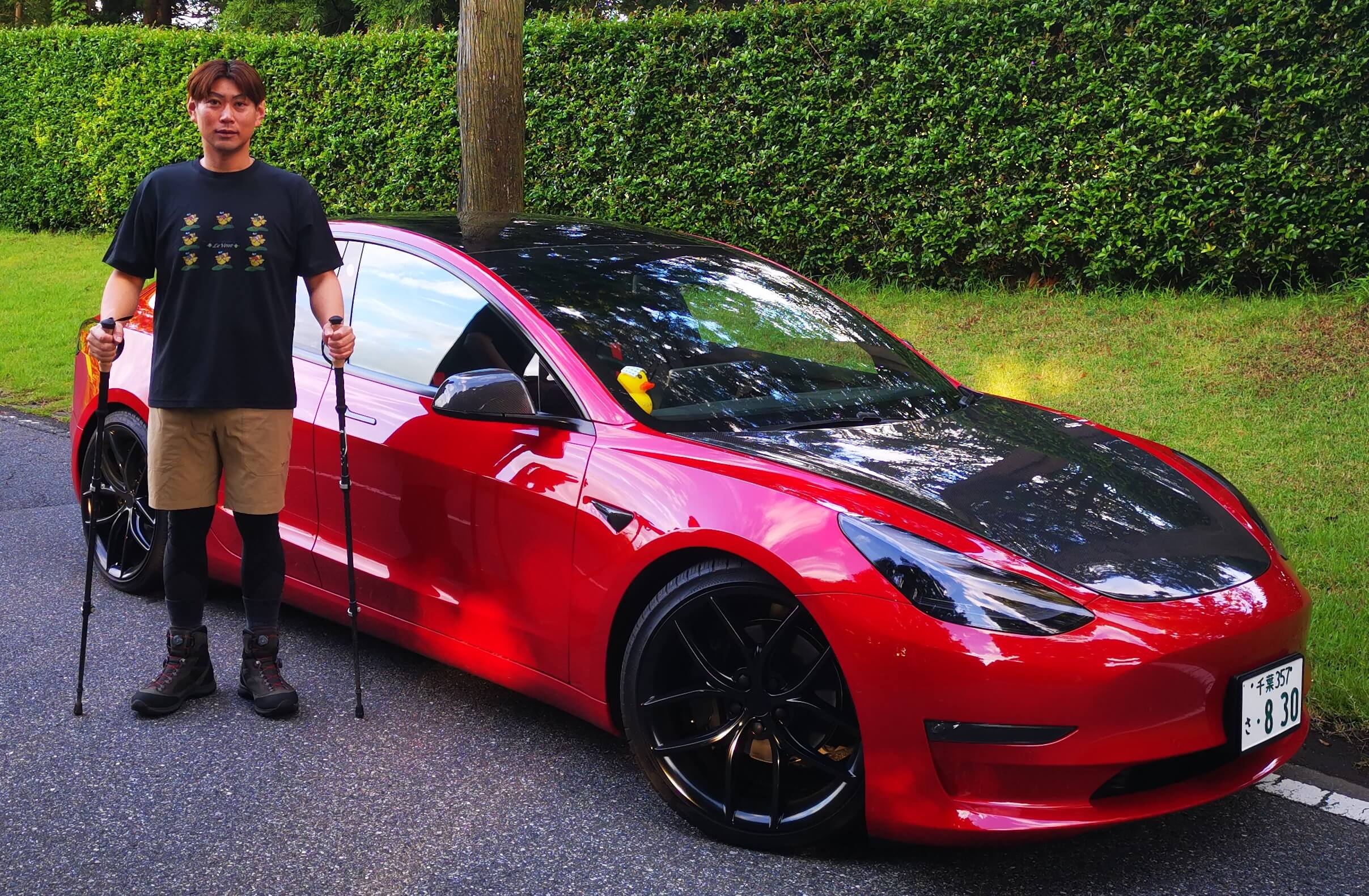 A Tesla Owner standing next to Red Model 3 with hiking poles 