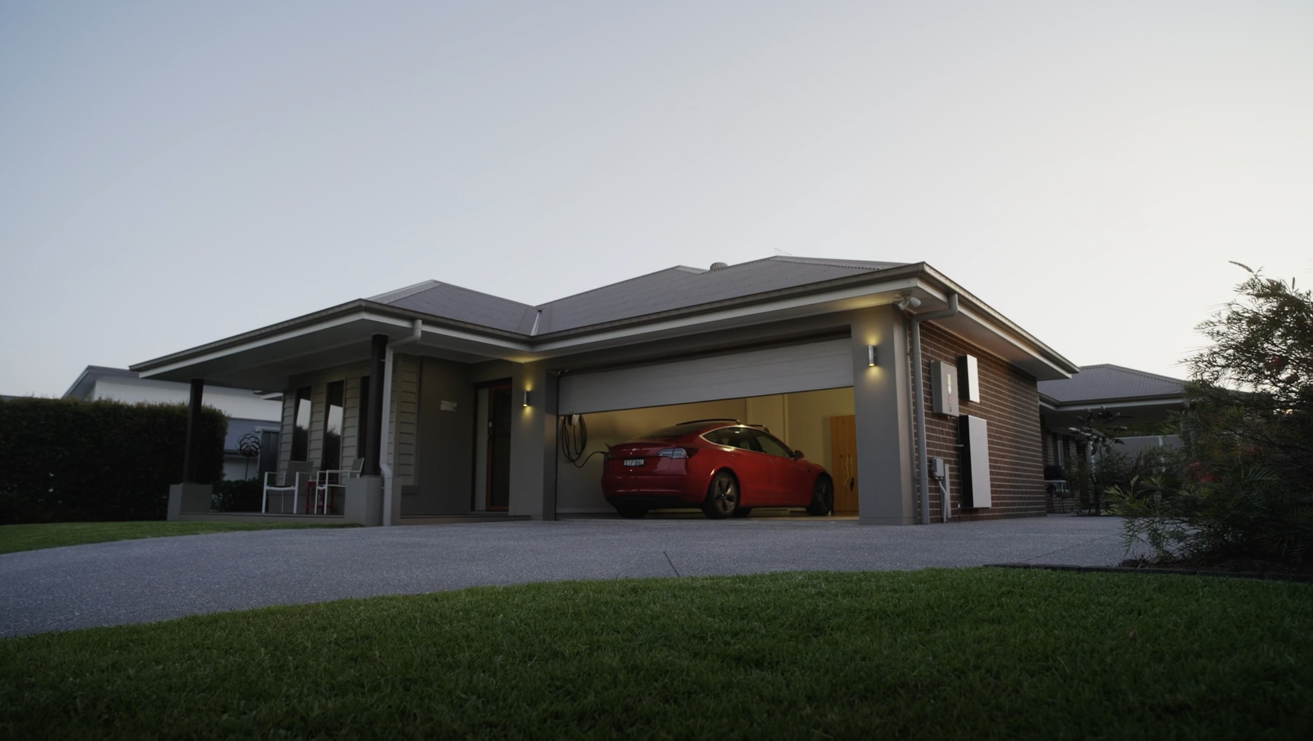 Home with Red Tesla Model 3 parked in a garage and Powerwall 2 installed outside