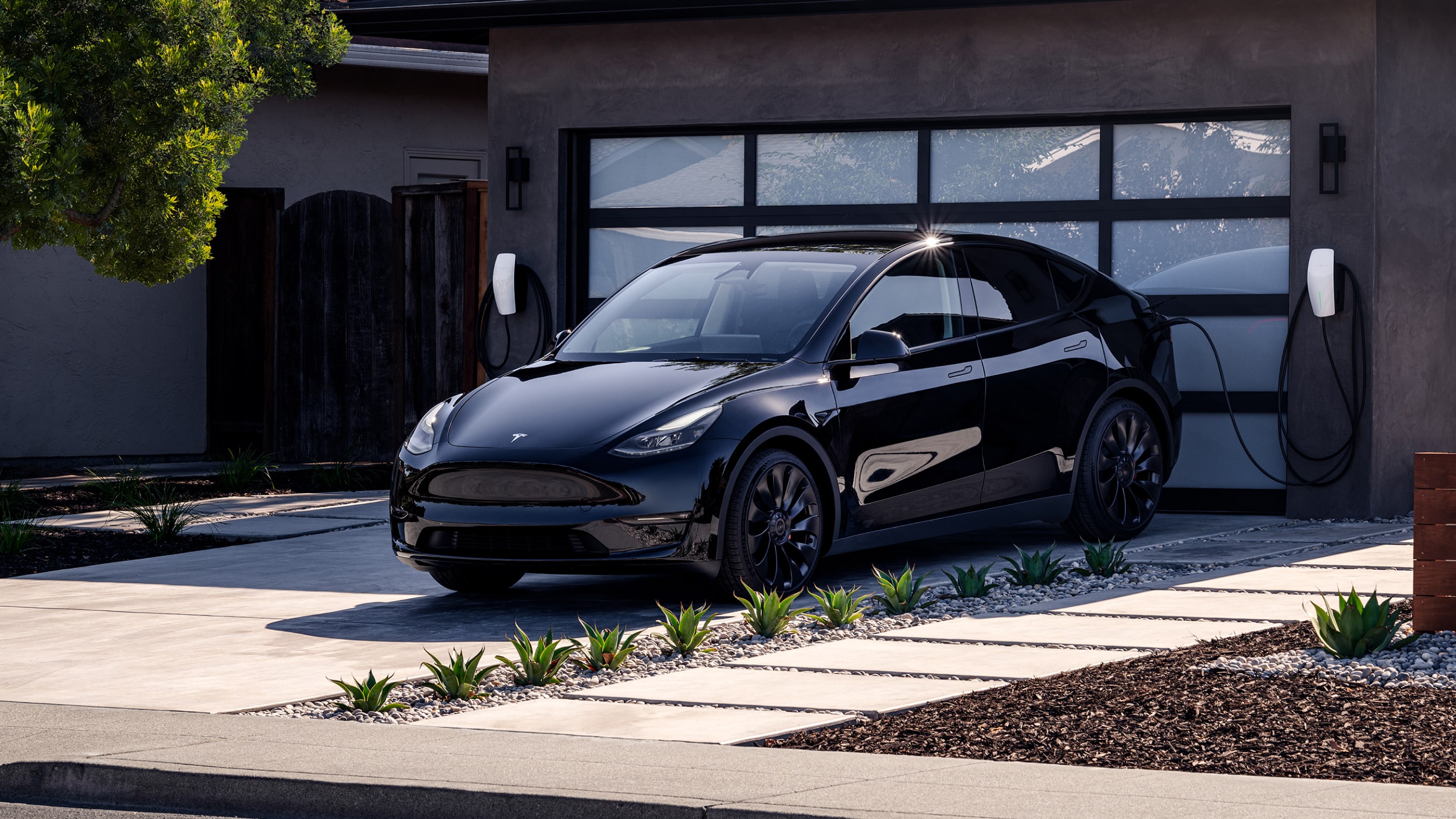 Black Model Y charging with a Wall Connector in front of a residential garage