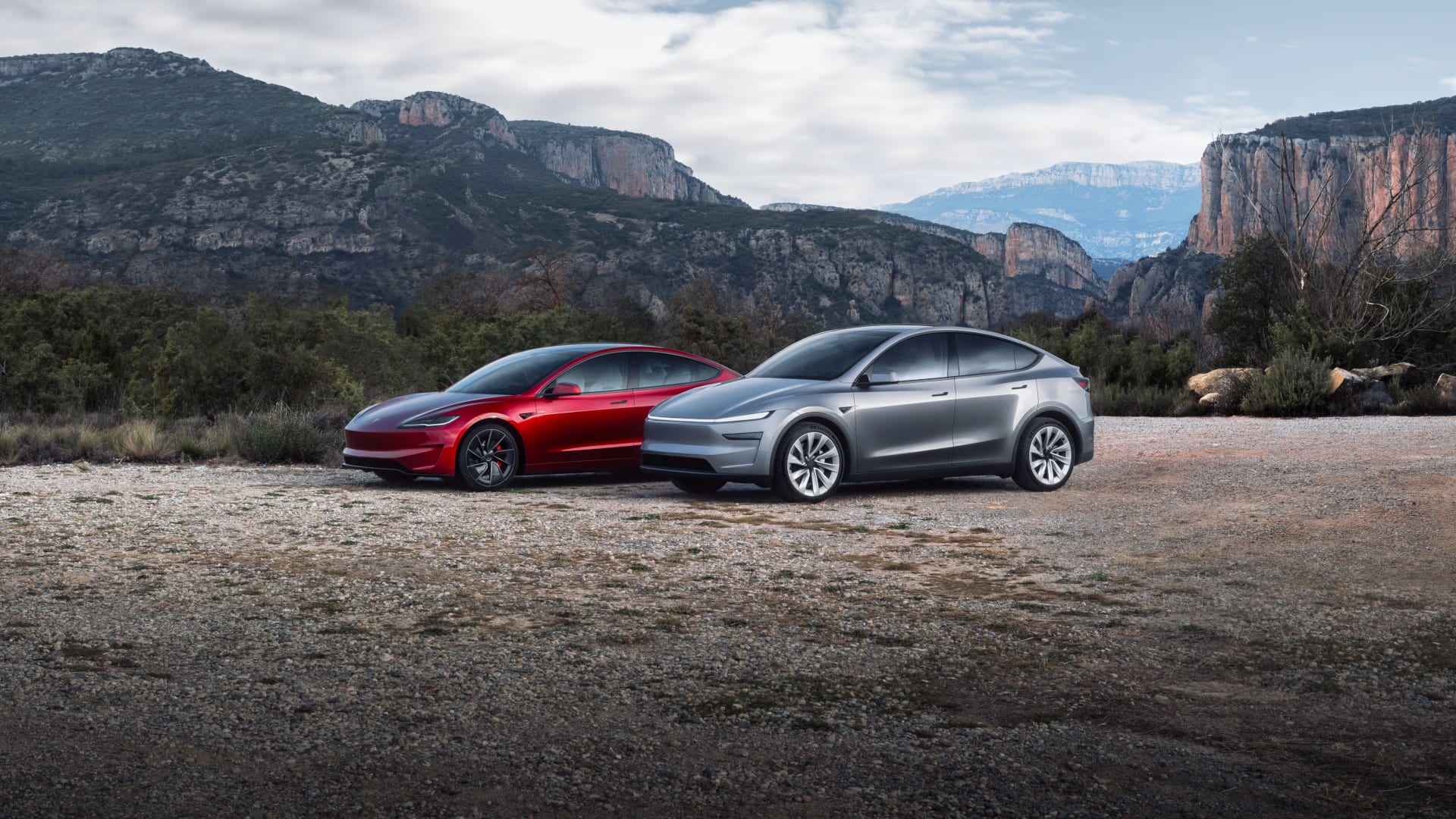 A red Model 3 and a silver Model Y parked in front of a mountainous landscape