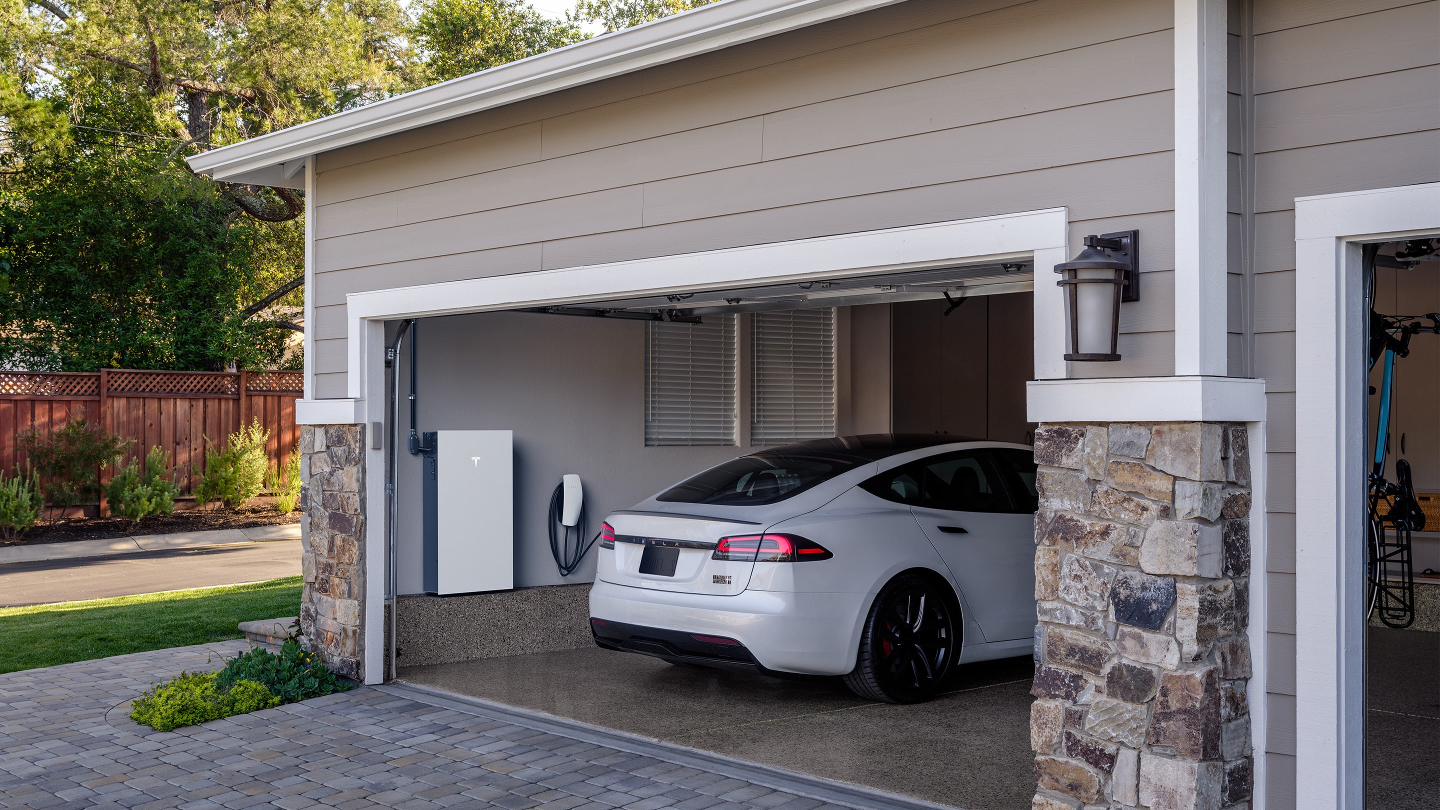 White Model S Plaid parked in a garage with a Wall Connector and Powerwall 3