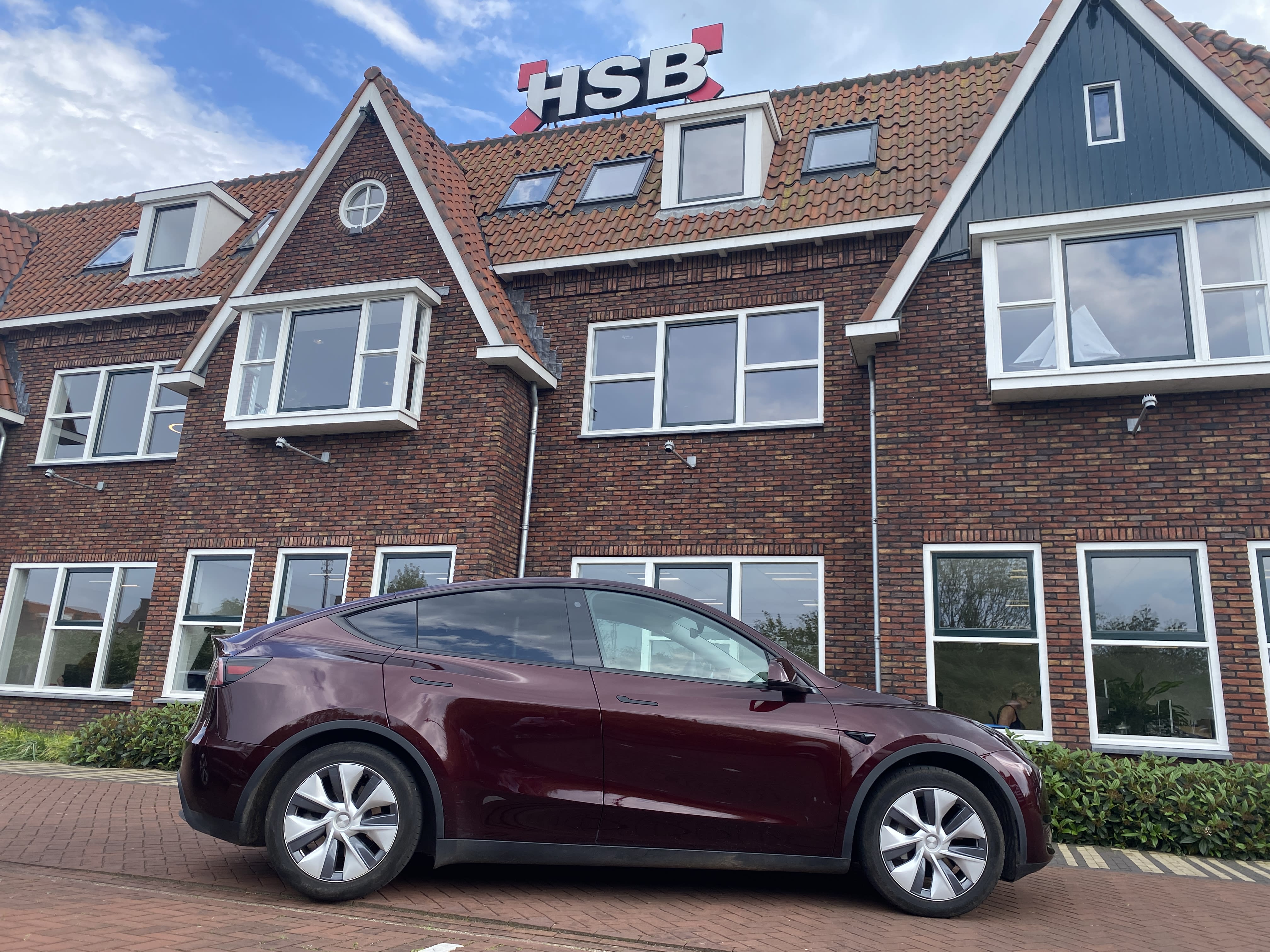 A Midnight Cherry Red Model Y parked in front of a brick building