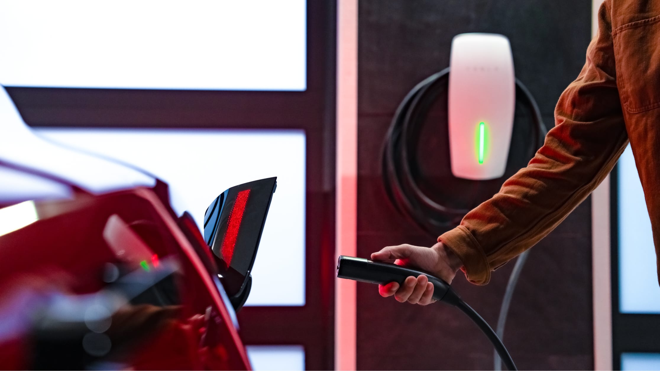 A hand holding a Wall Connector charge handle to charge a red Tesla vehicle