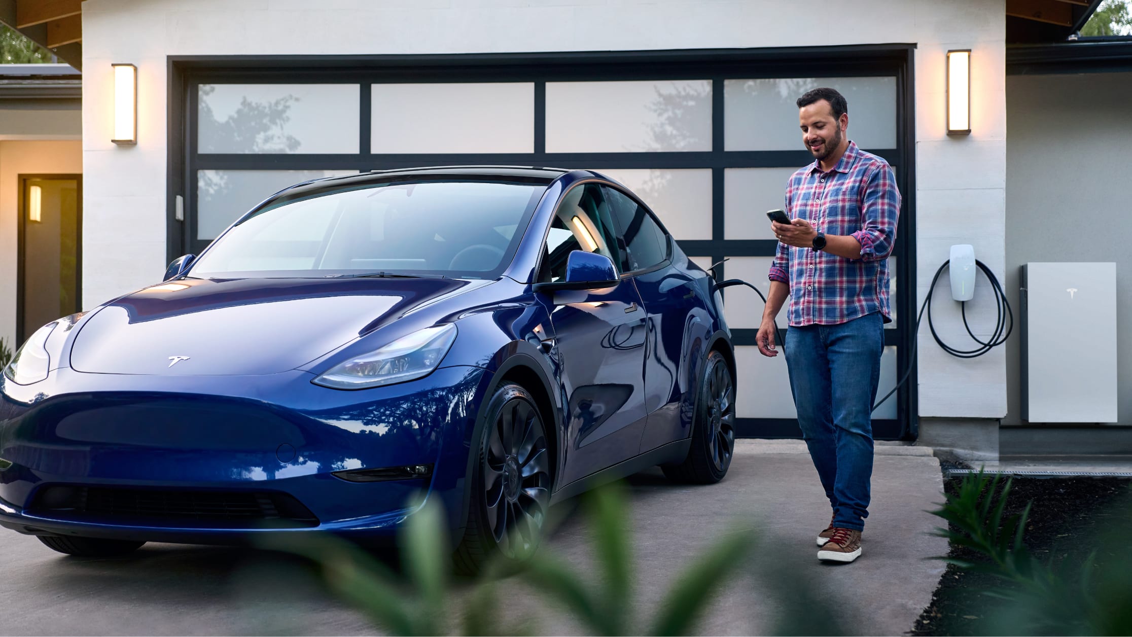 A man standing next to a blue Tesla vehicle while looking at his phone