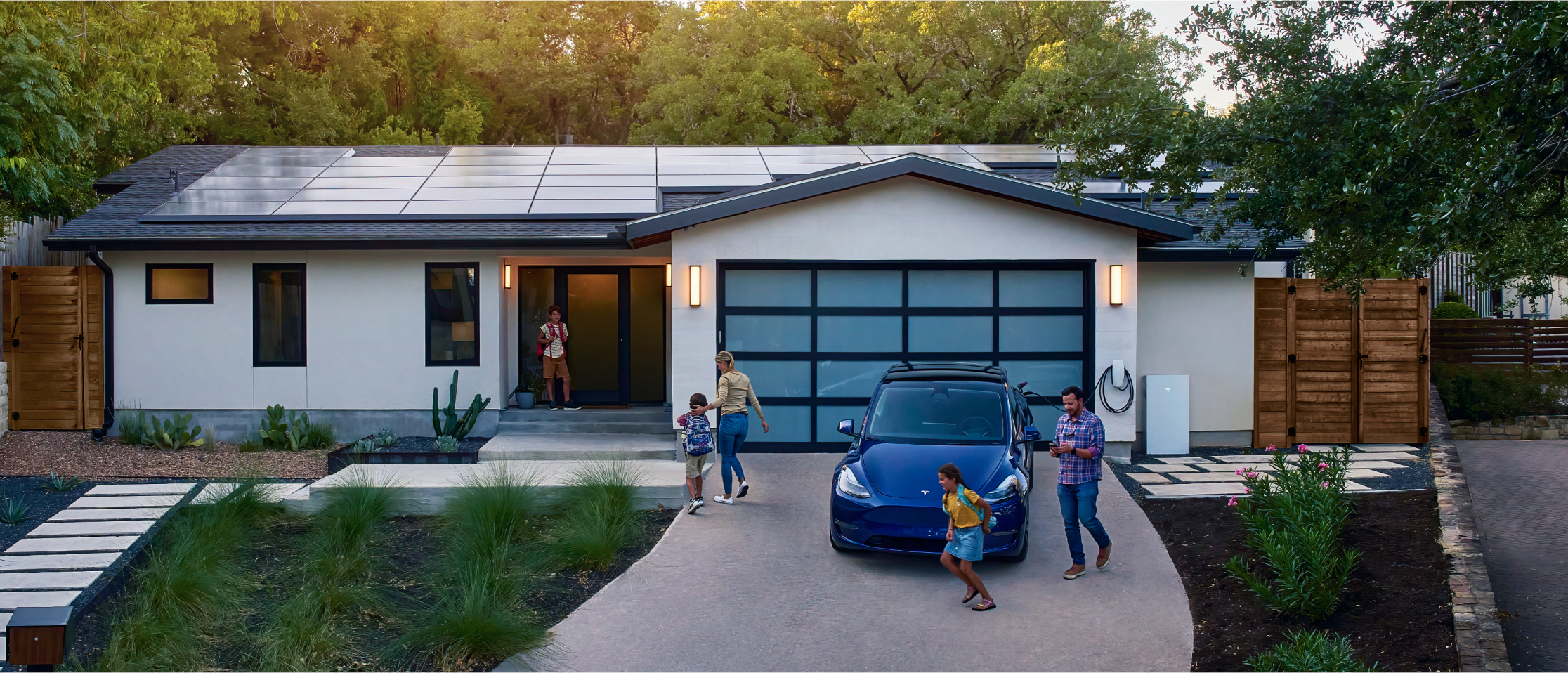 Family in front of a home with solar panels, Powerwall and Wall Connector