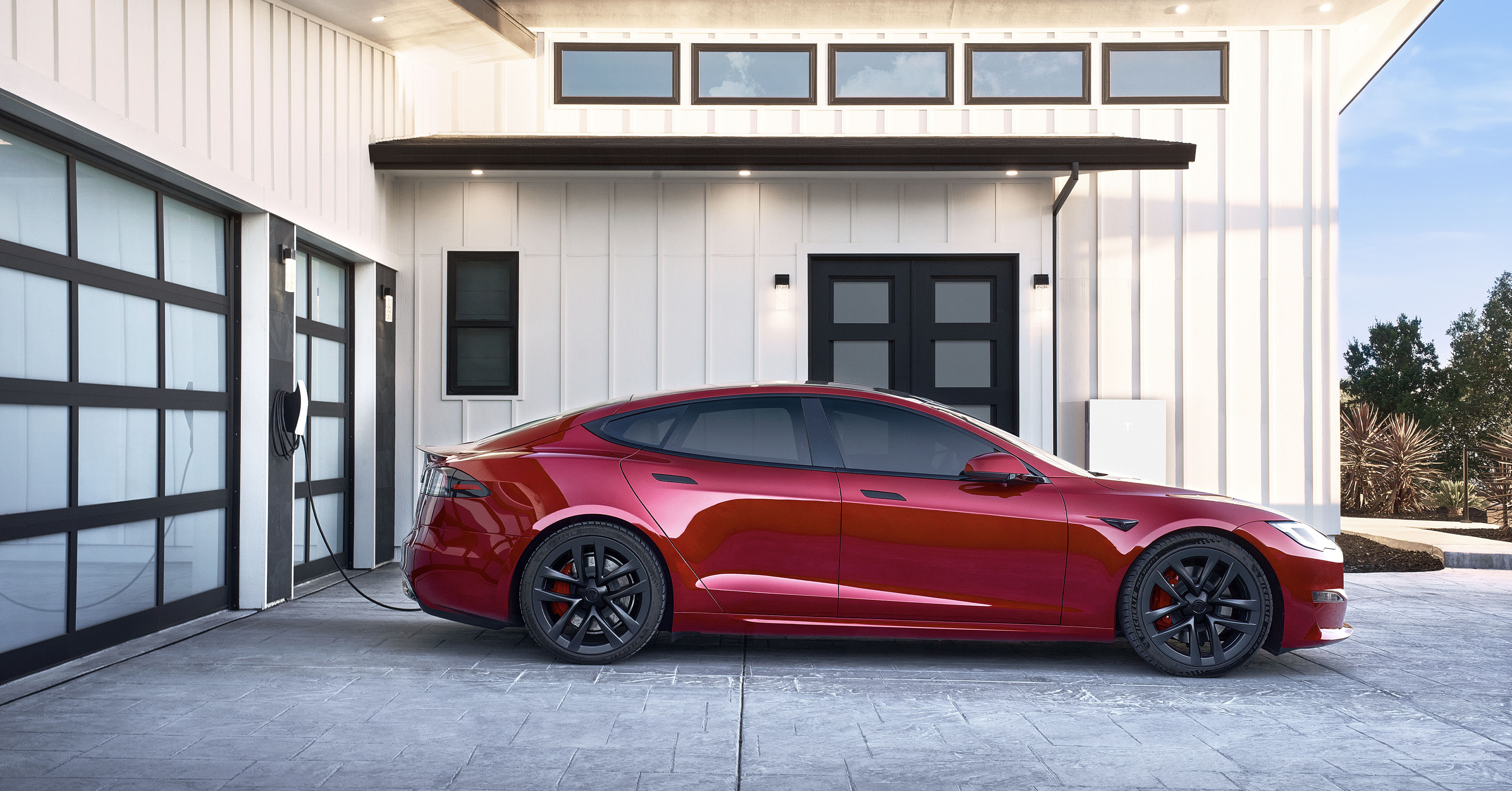 Red Model S charging with a Wall Connector and parked outside of a home with a Powerwall 3