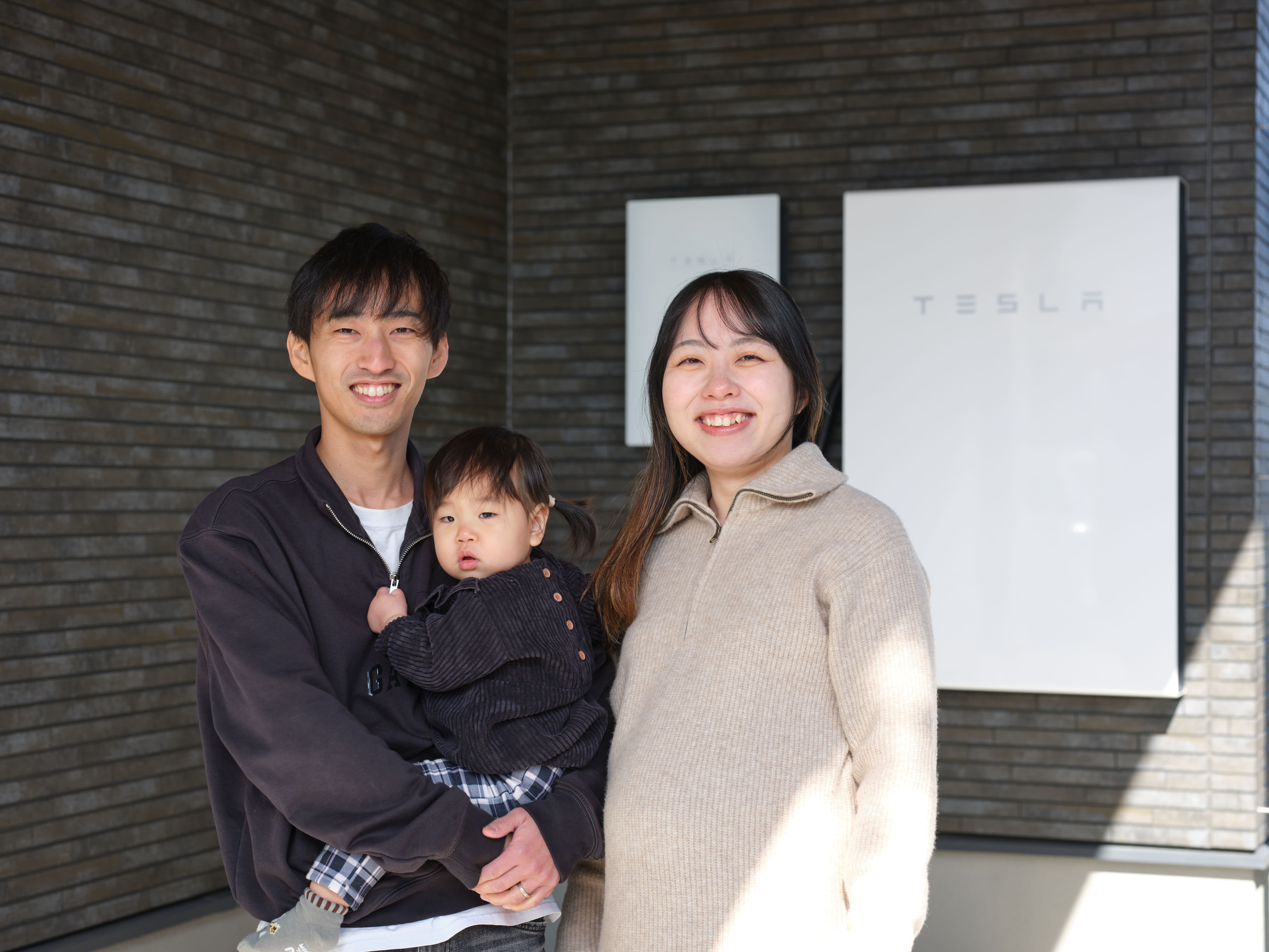 Family of three standing in front of a Tesla Powerwall