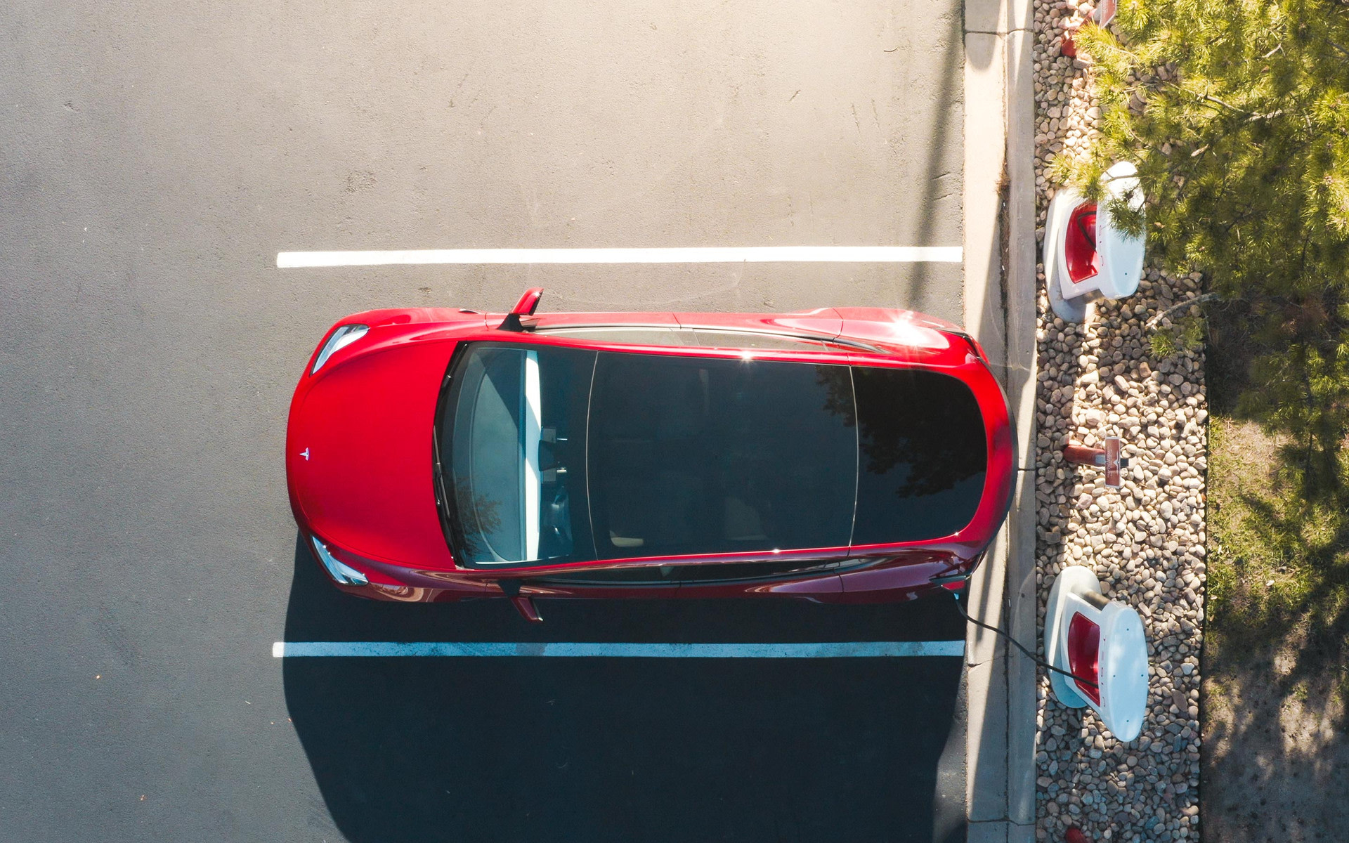 Bovenaanzicht van een rode Tesla die wordt opgeladen via een Supercharger