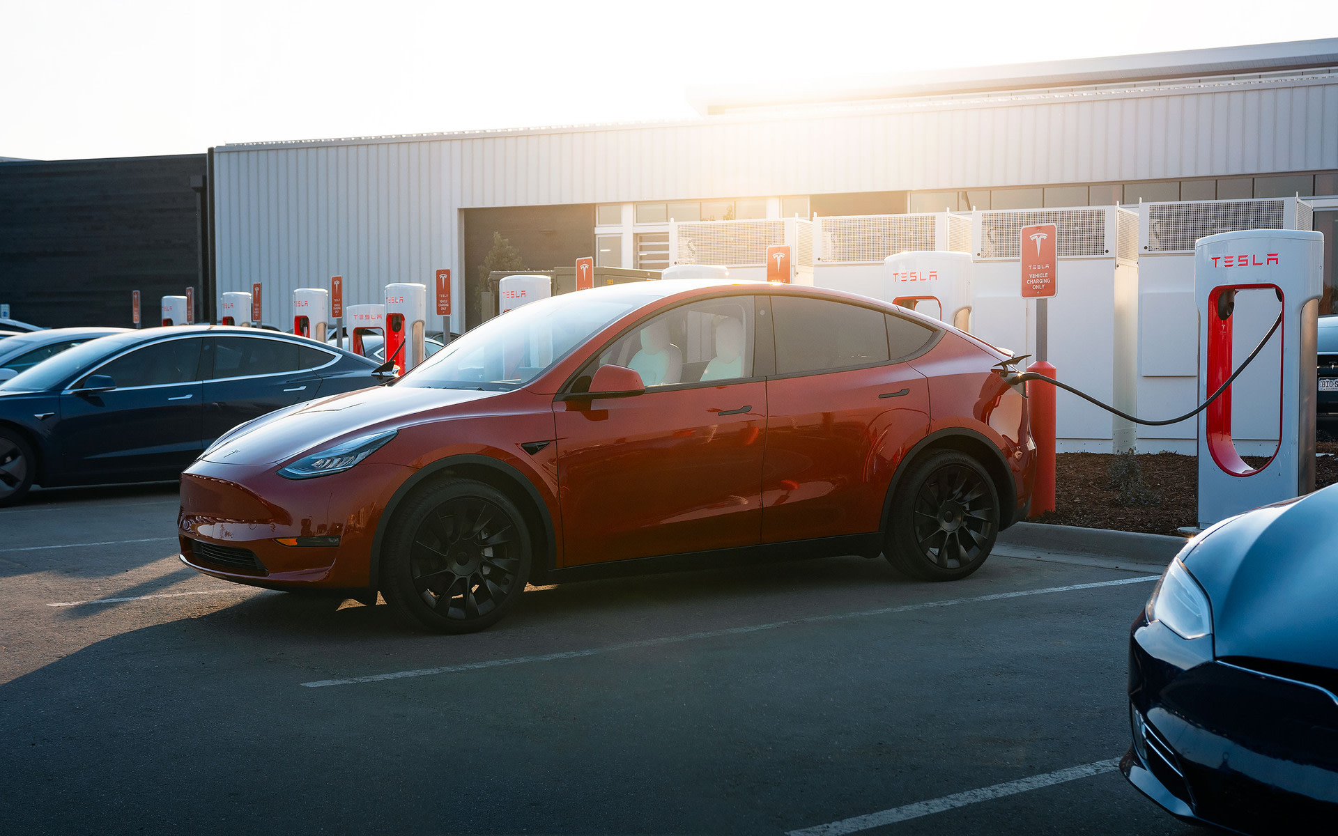 Red Model Y charging via Supercharger in a parking lot