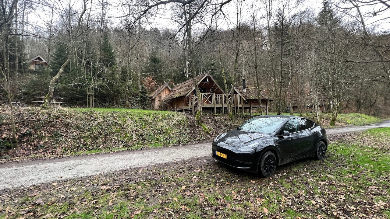 Solid Black Model Y Long Range geparkeerd in het bos voor een boomhut