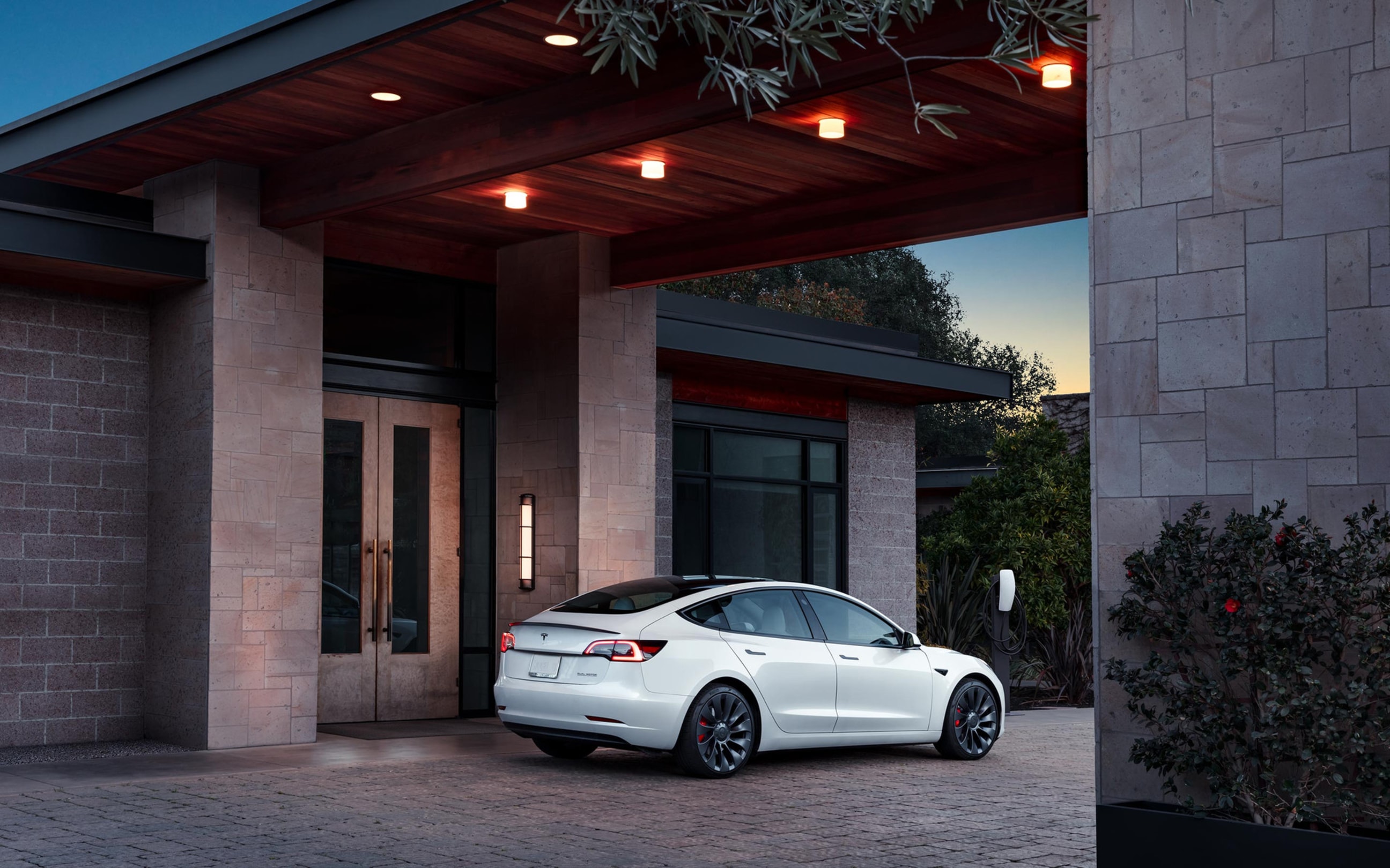 White Model 3 with Destination Charger parked in front of a hotel lobby