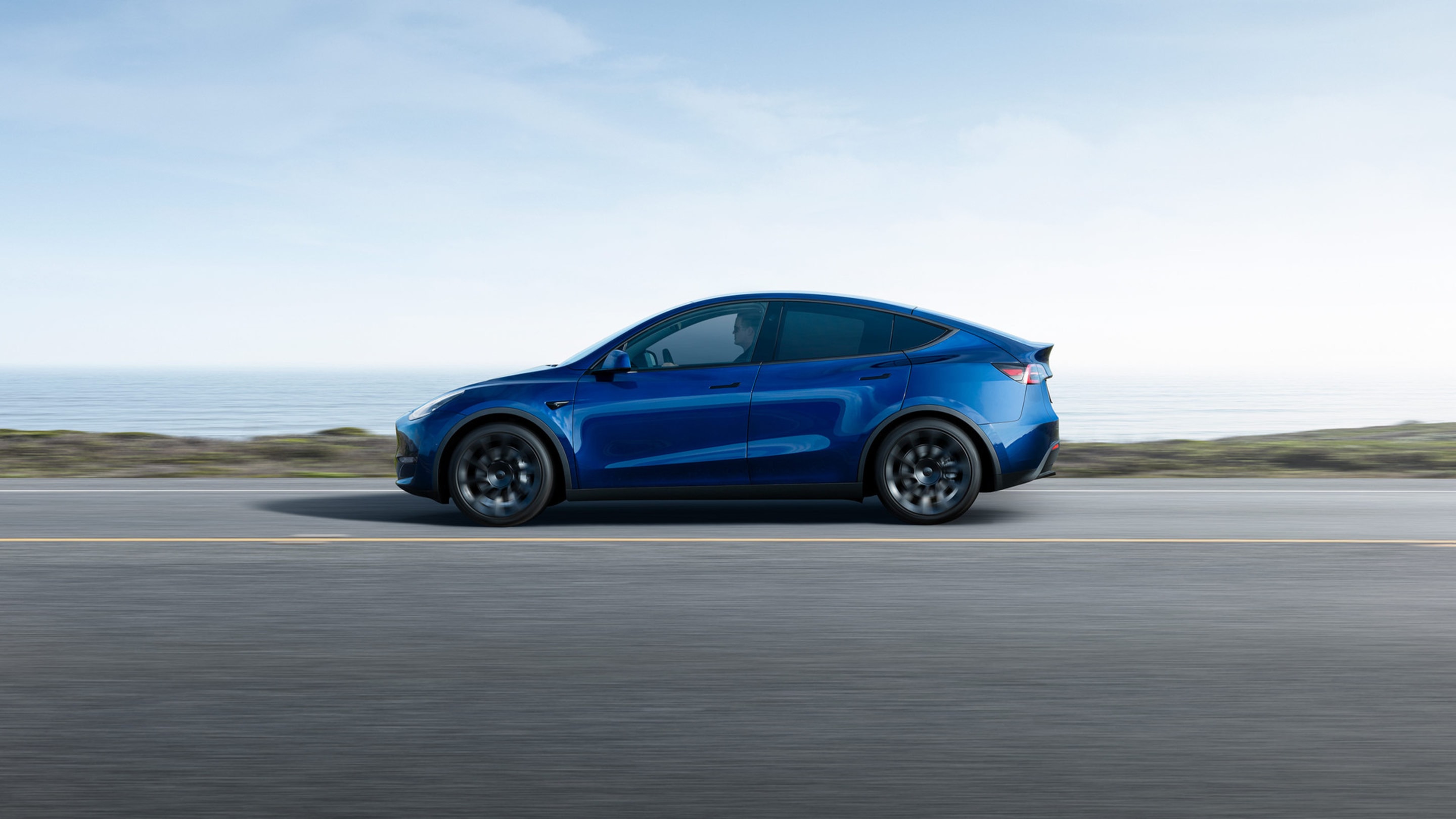 Blue Model Y accelerating down a waterfront road