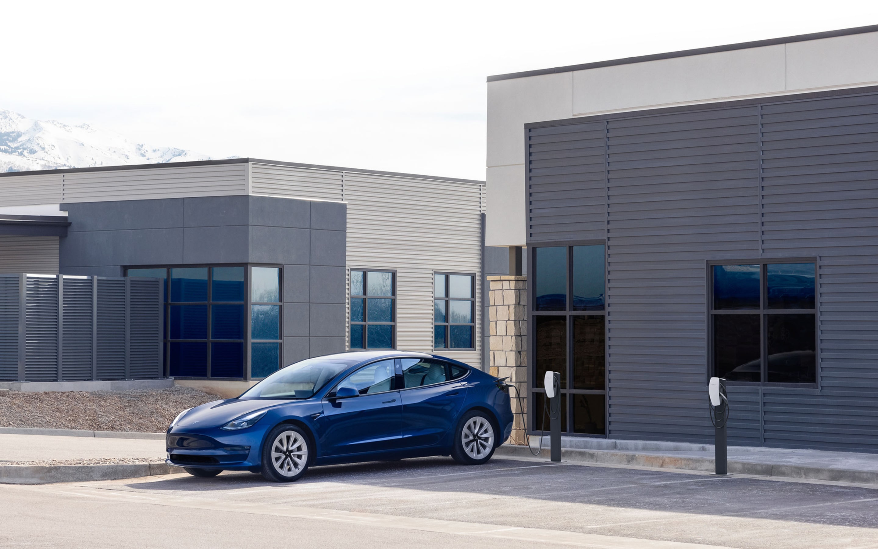 A blue Model 3 charging at a Wall Connector surrounded by industrial buildings