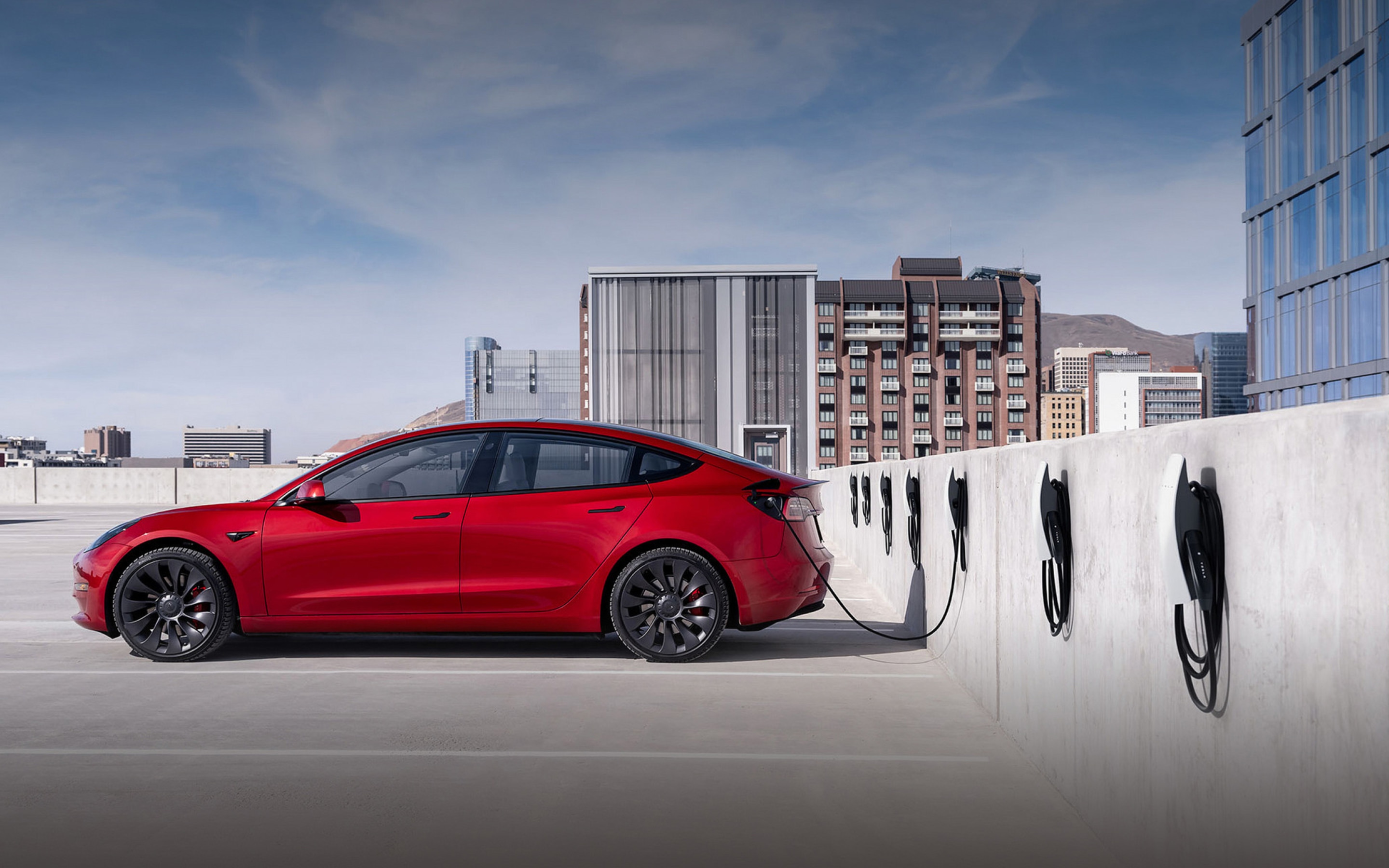 A red Model 3 Performance charging in a parking lot surrounded by skyscrapers