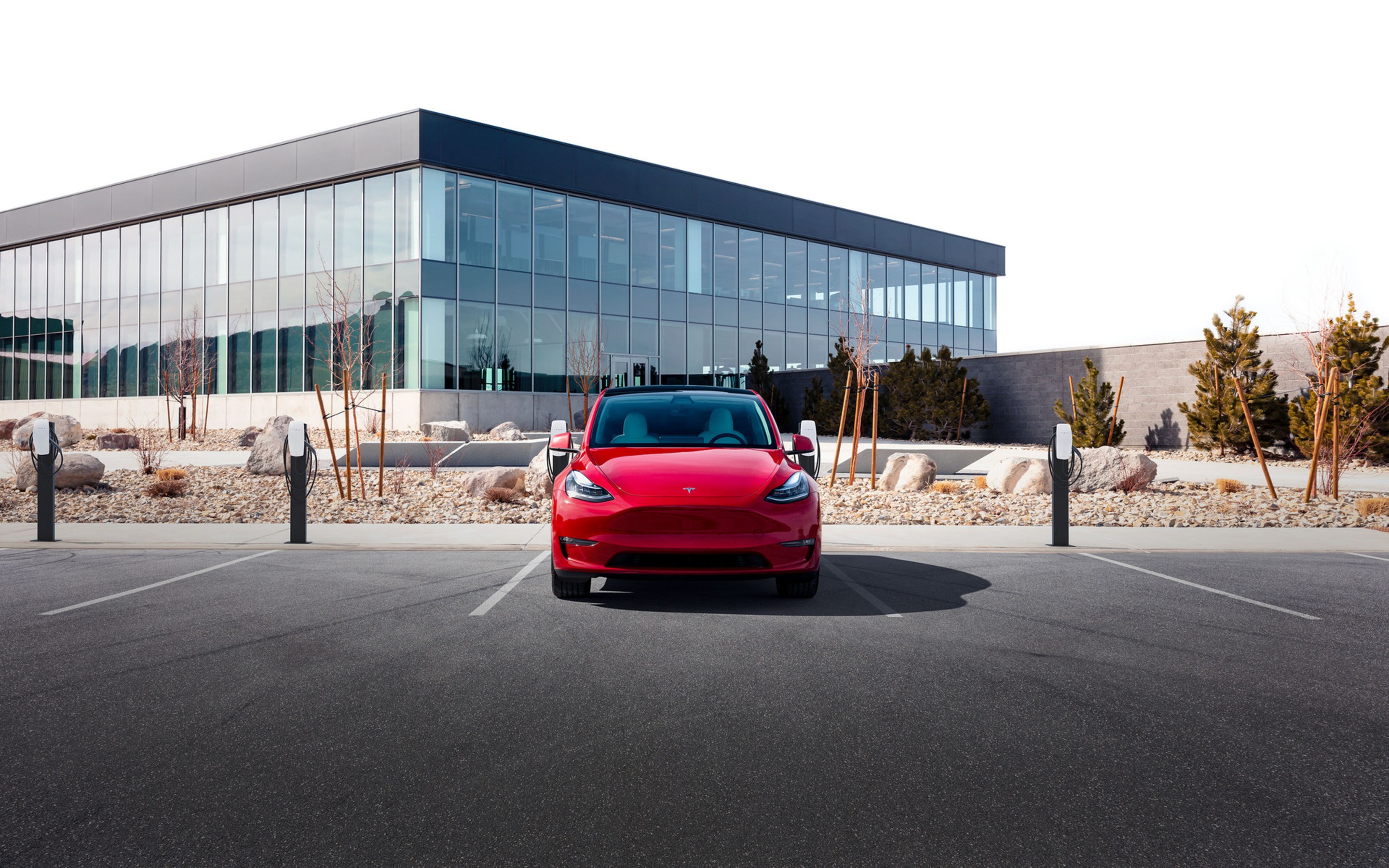 A red Model 3 parked next to multiple Wall Connectors in front of an office building