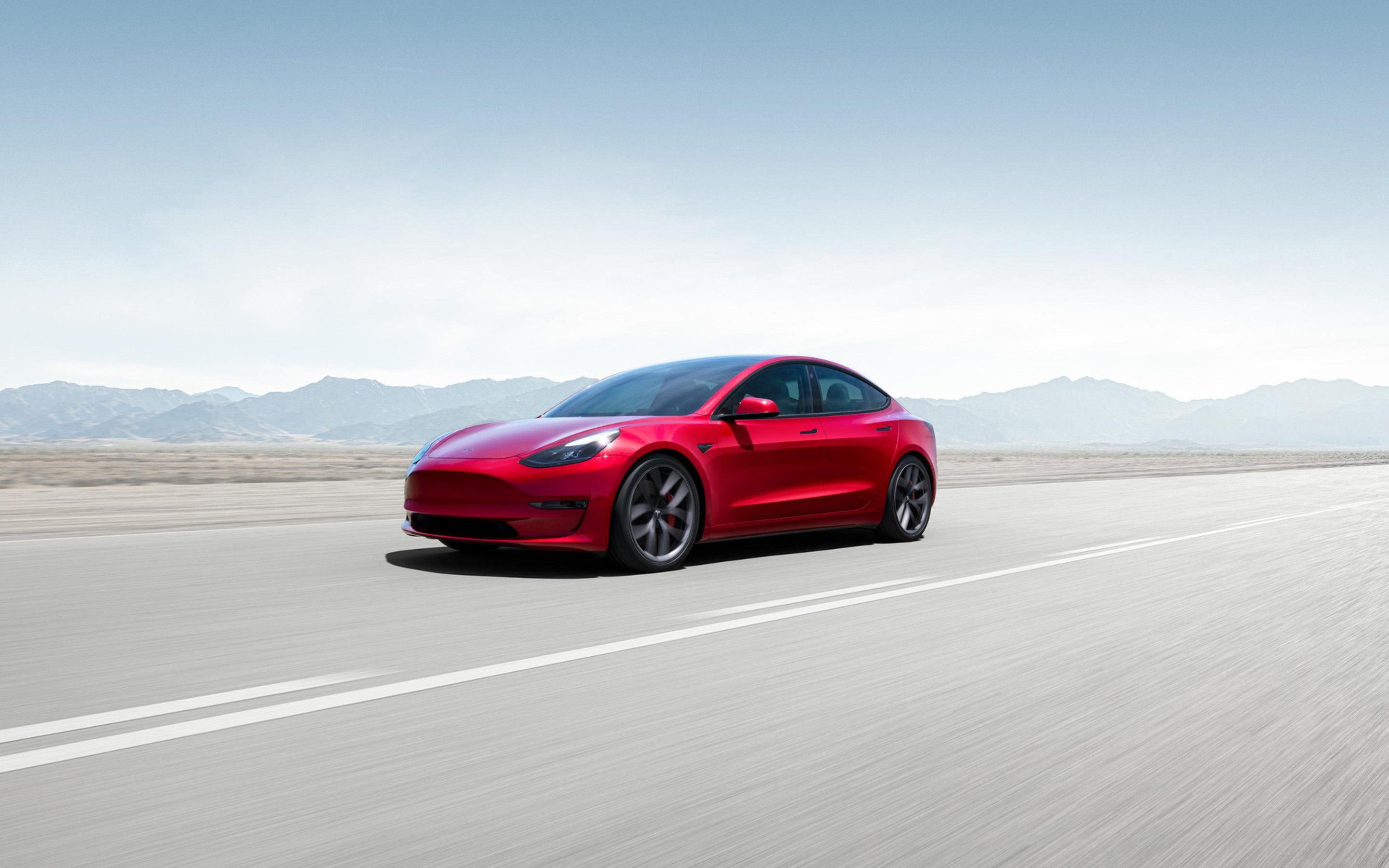 红色 Model 3 行驶在干燥的沙漠公路上