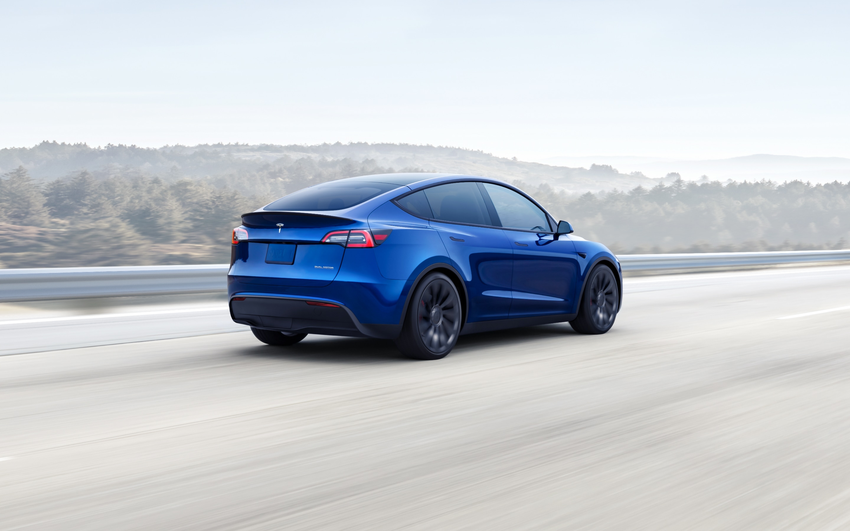 Metallic blue Model Y driving down a hillside highway