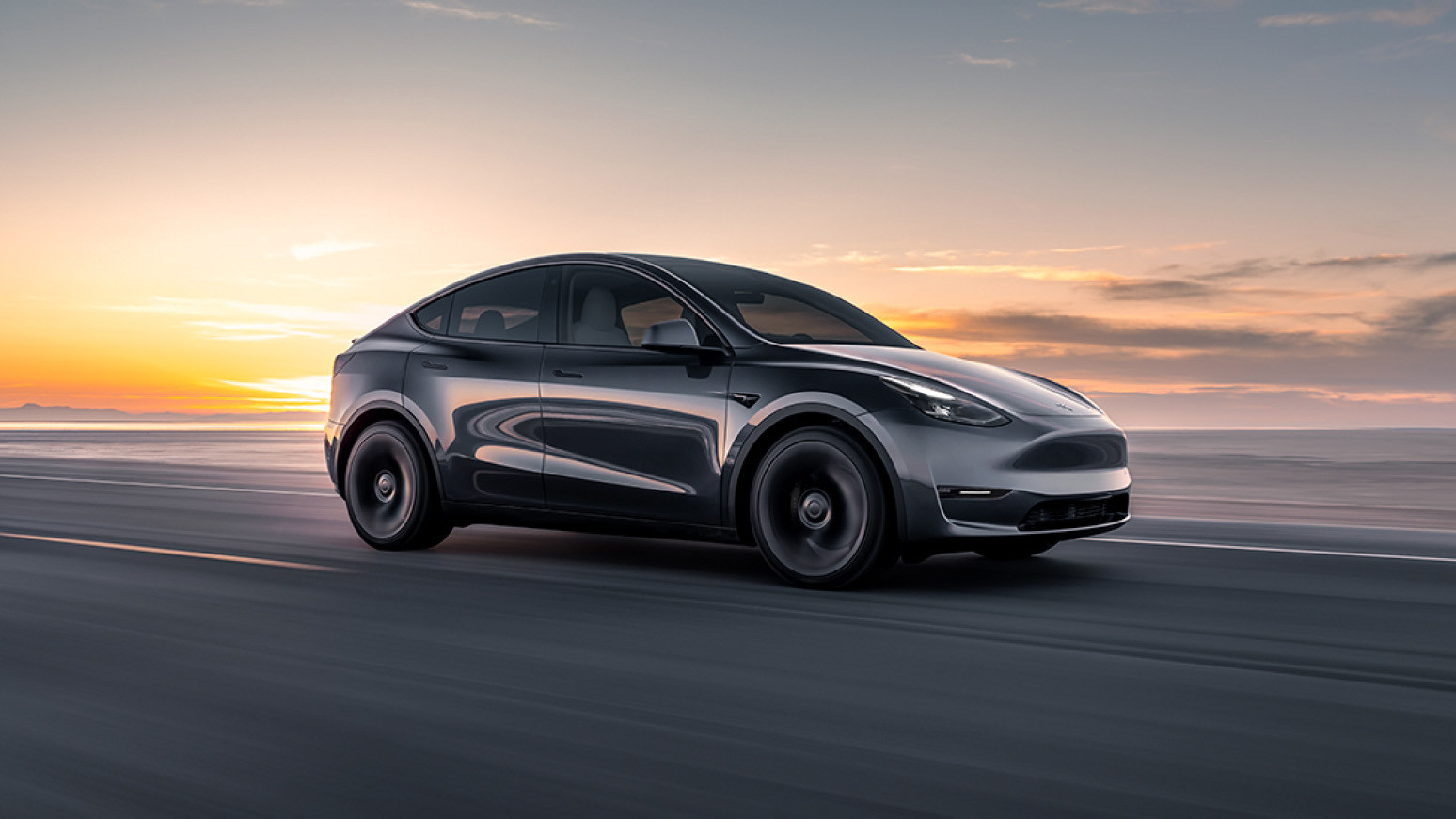 En grå Model Y som akselererer langs vannkanten i solnedgangen